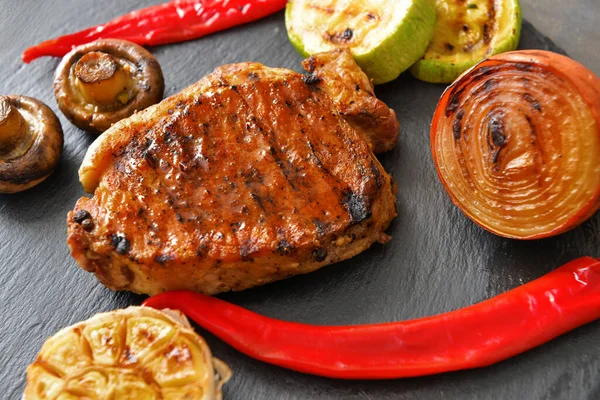 Cooked pork steak and vegetables on slate plate, closeup