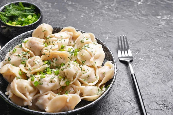 Bowl with tasty dumplings and herbs on dark background