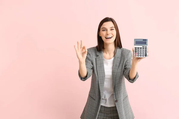 Young woman with calculator showing OK on color background