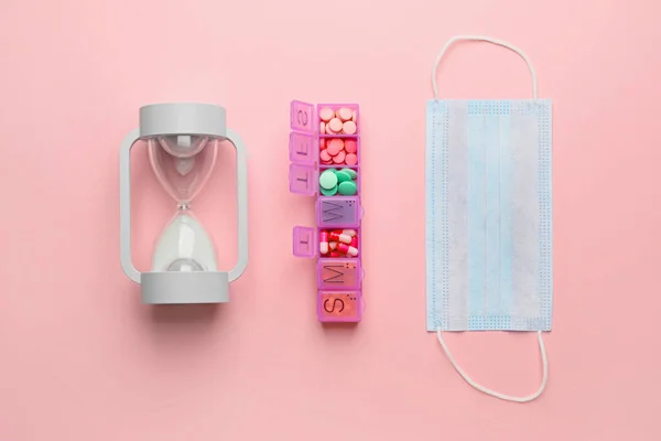 Hourglass, container with pills and mask on color background