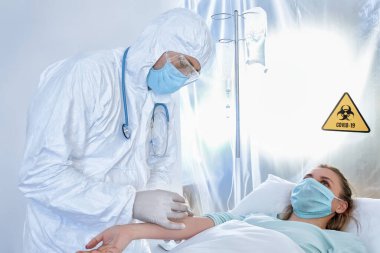 Biyolojik tehlike kıyafetli doktor bulaşıcı izolasyon koğuşunda hastayla çalışıyor. Coronavirüs salgını kavramı