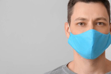 Gri arka planda koruyucu tıbbi maskeli bir adam.
