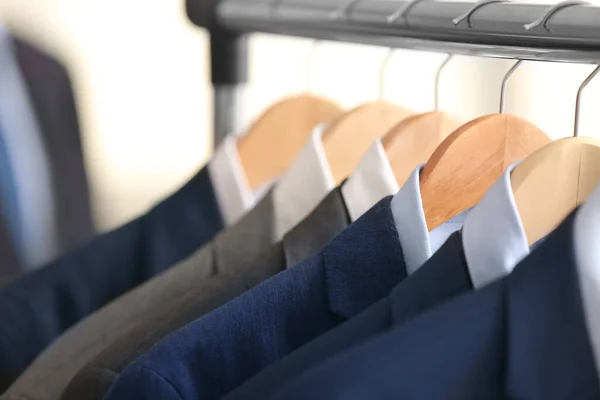 Hanger with different stylish male suits in store, closeup