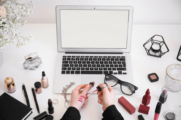 Woman with makeup cosmetics sitting at table with laptop