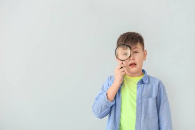 Gri arka planda büyüteci olan şirin bir okul çocuğu.