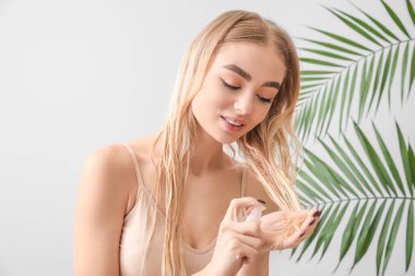 Genç kadın gri arka planda saç için kozmetik kullanıyor.