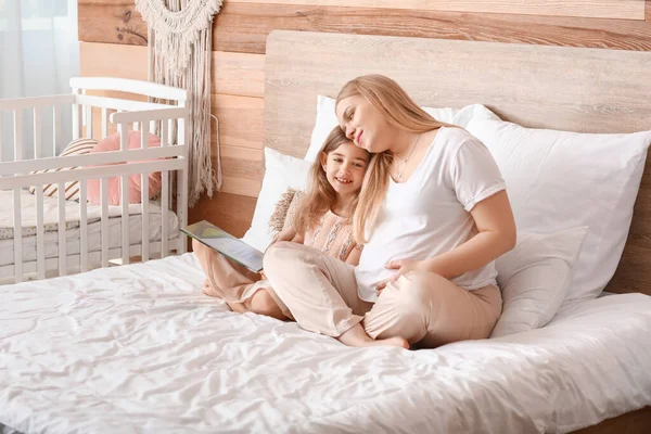 美しいです妊娠中の女性と彼女の小さな娘読書本でベッドルーム — ストック写真