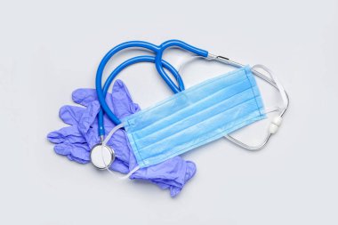 Tıbbi maske, steteskop ve arka planda lastik eldivenler.