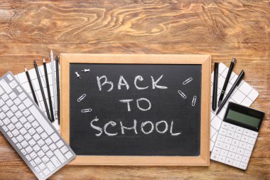 Malzeme seti, bilgisayar klavyesi ve tahta zemin üzerinde okula geri dönen yazı tahtası