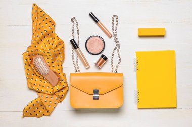 Kadın aksesuarları ve beyaz ahşap arka planda not defteri olan şık bir çanta.