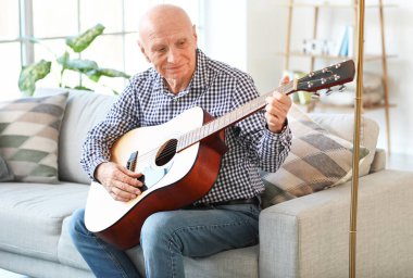 Evde gitar çalan yaşlı bir adam.