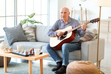 Evde gitar çalan yaşlı bir adam.