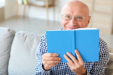 Evde kitap okuyan yaşlı bir adam.