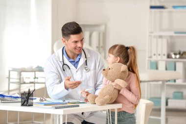 Pediyatrist küçük kıza klinikte termometreyi nasıl kullanacağını gösteriyor.