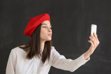 Güzel genç bir kadın karanlık arka planda selfie çekiyor.