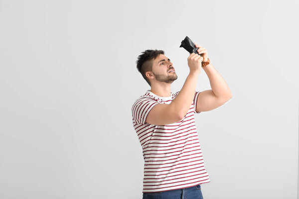 Sad man with empty purse on light background