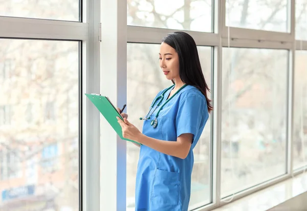 Female Asian doctor with clipboard in clinic