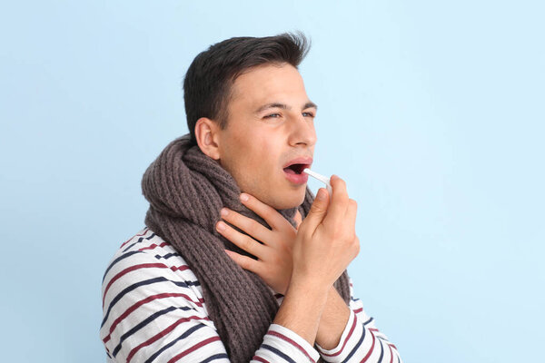 Ill young man with inhaler on light background