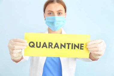 Koruyucu maskeli bir doktor elinde kağıt kağıtla arka planda metin QuarANTINE 'ı tutuyor. Salgın kavramı