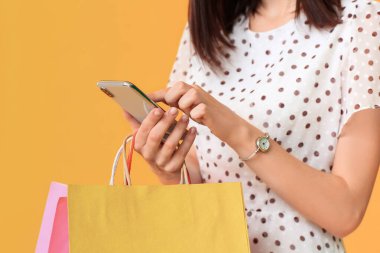 Alışveriş çantaları ve renkli arka planda cep telefonu olan güzel bir genç kadın.