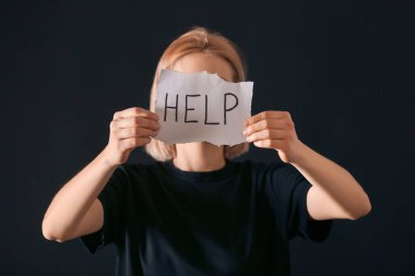Elinde kâğıt tutmakta olan bir kadın koyu arka planda yardım mesajı atıyor. Depresyon kavramı