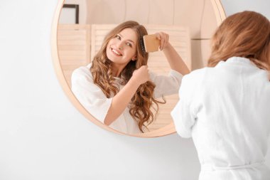 Güzel genç bir kadın banyoda saç tarıyor.