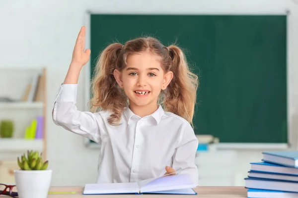 Søt Liten Skolepike Med Hevet Hånd Ved Skrivebordet Klasserommet – stockfoto