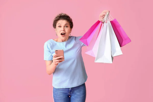 Verrast Jonge Vrouw Met Mobiele Telefoon Boodschappentassen Kleur Achtergrond — Stockfoto