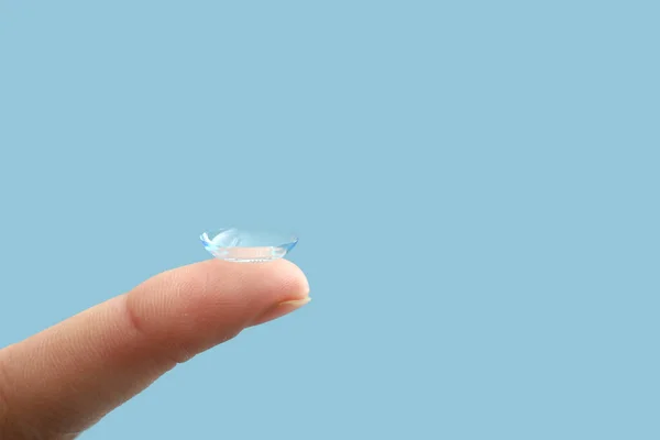 Female finger with contact lens on color background