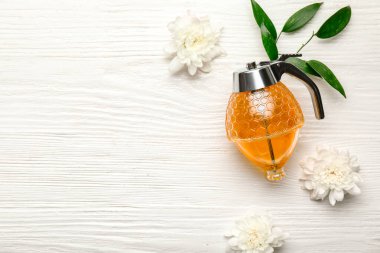 Tatlı bal kavanozu ve beyaz ahşap arka planda çiçekler.