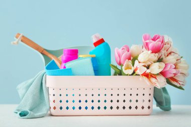 Renkli arkaplanda temizlik malzemeleri ve bahar çiçekleri.