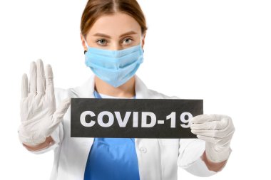 Beyaz arka planda COVID 19 yazılı kağıt çarşaf tutan koruyucu maskeli bir doktor. Salgın kavramı