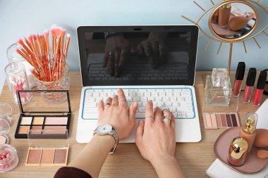 Kozmetik ve dizüstü bilgisayarlı makyöz masada oturuyor.