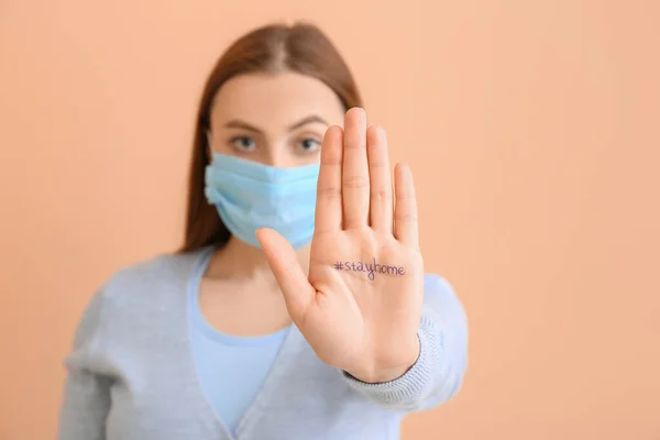 Woman in protective mask showing her palm with written text on color background. Concept of Coronavirus epidemic