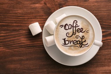 Bir fincan lezzetli kapuçino ve ahşap arka planda marşmelov.