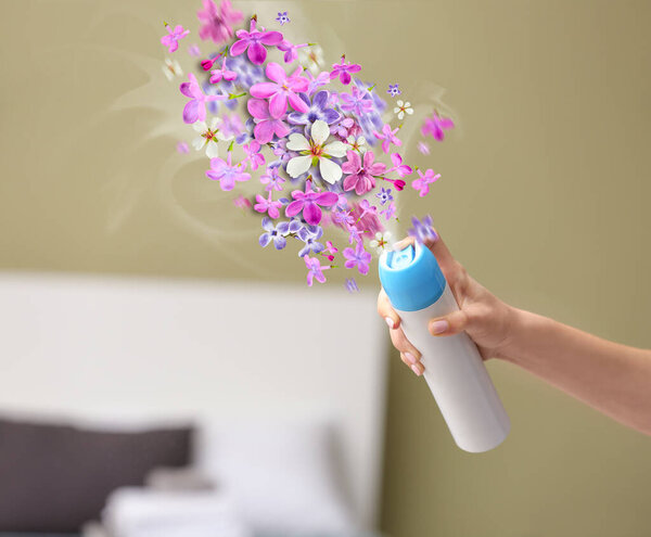 Woman spraying floral air freshener at home