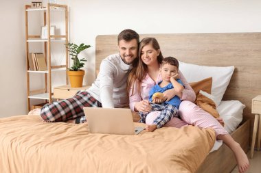 Yatak odasında dizüstü bilgisayar kullanan mutlu aile.