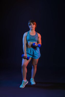 Koyu arka plan üzerinde dumbbells ile sportif kaslı kadın