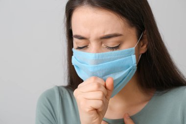 Gri arka planda tıbbi maske takan hasta genç bir kadın.