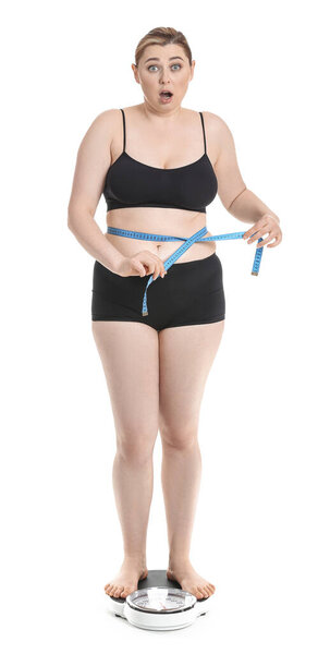 Shocked overweight woman standing on scales against white background. Weight loss concept