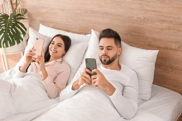 Pareja Joven Con Teléfonos Móviles Acostados Cama Casa —  Fotos de Stock