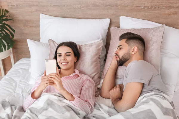 Young couple with mobile phone lying in bed at home