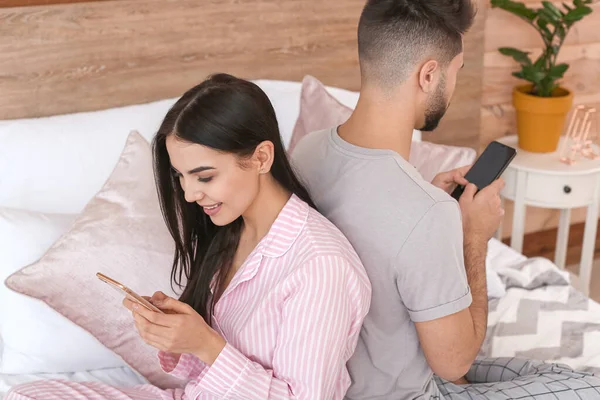 Young couple with mobile phones sitting on bed at home