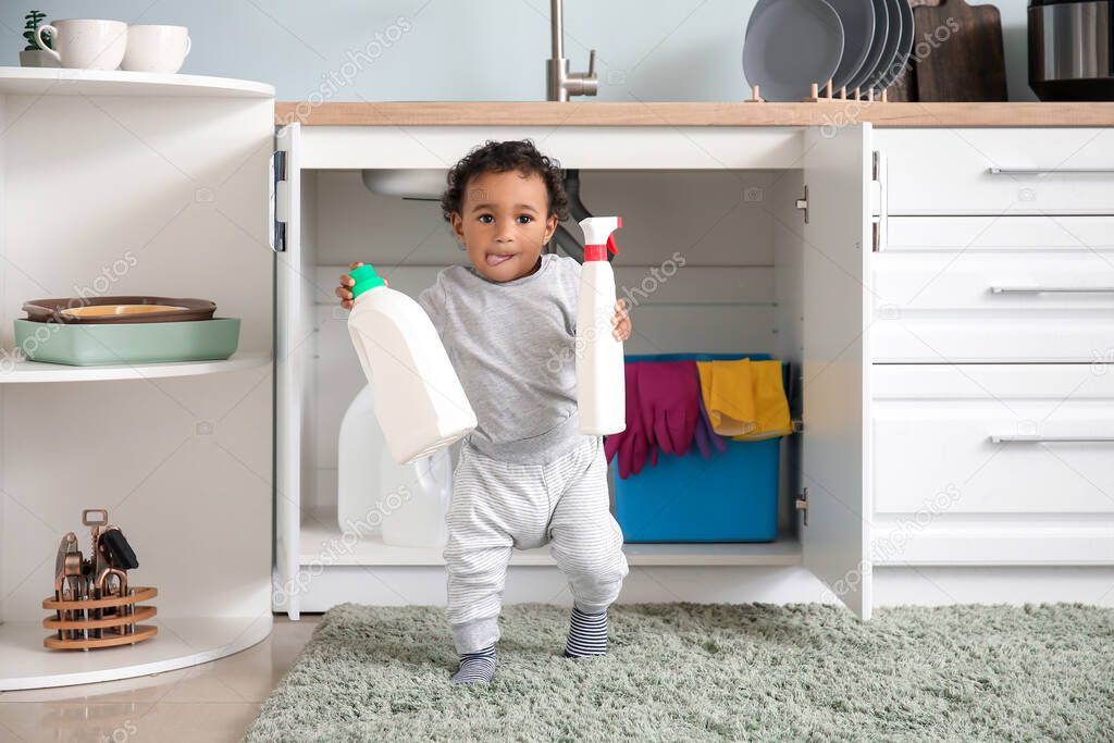 Little African-American baby playing with detergents at home. Child in danger