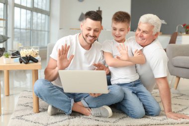 Babası ve oğluyla evde dizüstü bilgisayar kullanan bir adam.
