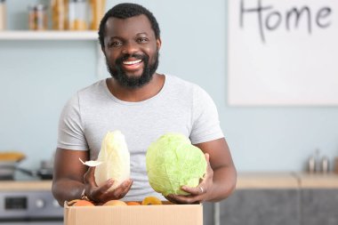 Afro-Amerikalı adam mutfaktaki marketten taze ürünleri indiriyor.