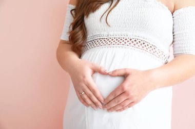 Güzel hamile kadın, elleri renk arkaplanda kalp yapıyor, yakın plan.