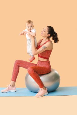 Genç sportif anne ve bebeği renk arka planında fitball ile egzersiz yapıyorlar.