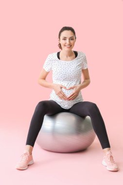 Genç hamile kadın renk arka planında fitball ile egzersiz yapıyor.