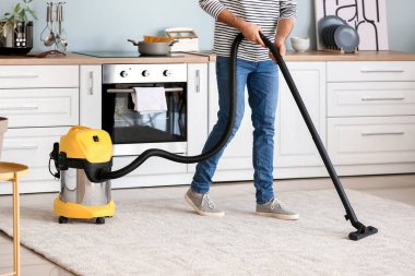 Genç adam mutfakta yerleri süpürüyor.